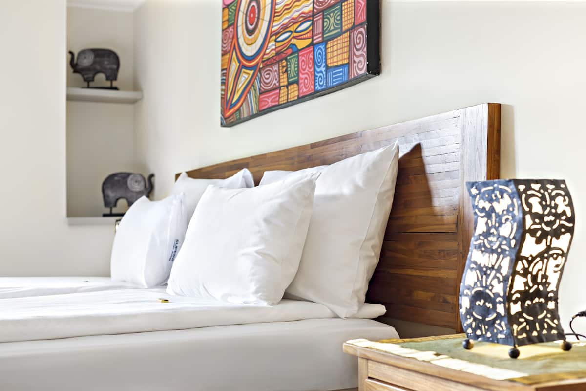 A bed with white bedding, a wooden headboard, and a colorful abstract painting above it.
