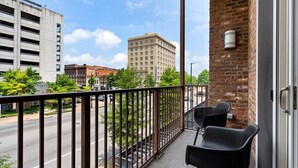 Un balcon avec deux chaises noires, un mur de briques et une vue sur une rue de la ville et des immeubles.
