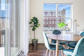 Enjoy meals in this stylish dining area with a round table and four chairs, surrounded by a potted plant and large windows offering a city view.