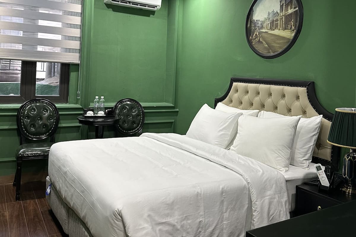 A neatly arranged bedroom with a large bed, a round mirror, a small table with bottles, and a chair.