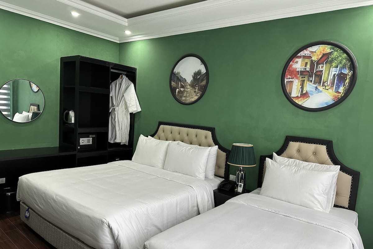 A hotel room with two beds, a wardrobe, a mirror, and artwork on the walls.