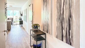 Een moderne hal met een groot abstract schilderij, een klein tafeltje met een plant, en uitzicht op een eetgedeelte.