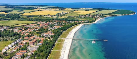 Luftaufnahme einer Küstenstadt mit Strand, Häusern und einem Steg.