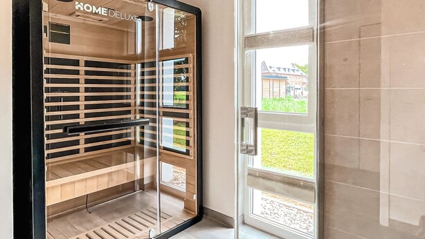 Een moderne badkamer met een glazen douchecabine, een houten wastafelmeubel en een glazen deur met uitzicht op een tuin.