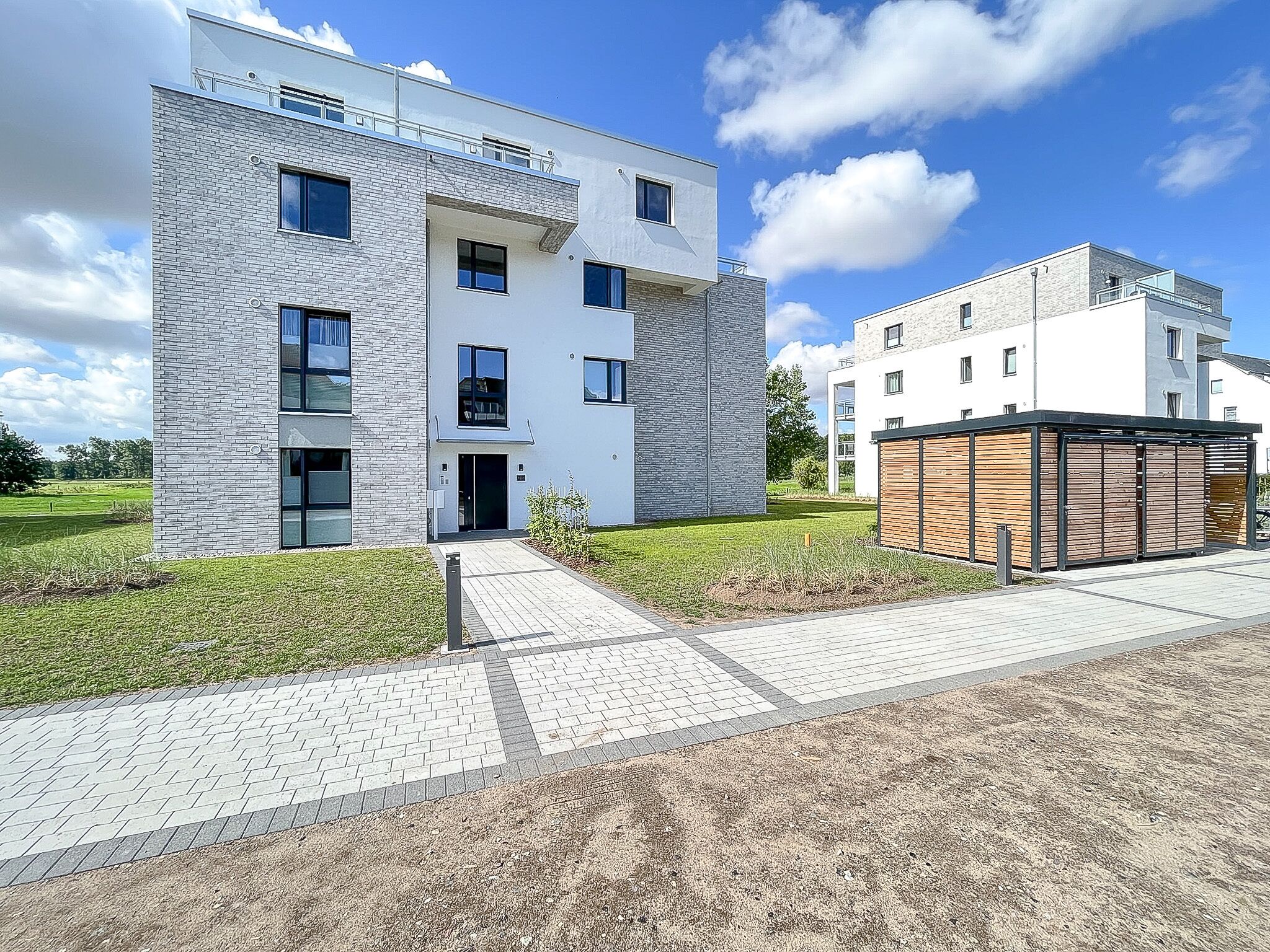 Um edifício moderno de vários andares com telhado plano, janelas grandes e área de entrada pavimentada.