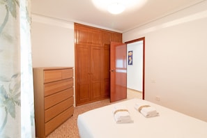 A bedroom with a wooden wardrobe, a bed with two towels, and a door leading to another room.