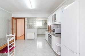 A kitchen with white cabinets, a refrigerator, a microwave, and a dining area with a chair and table.
