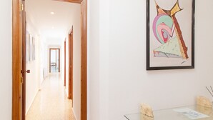 Un couloir avec une table et des chaises en verre, une œuvre d’art abstraite encadrée au mur et une porte donnant sur une autre pièce.