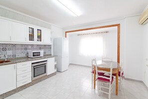 A kitchen with white cabinets, a microwave, a refrigerator, and a dining area with a table and chairs.