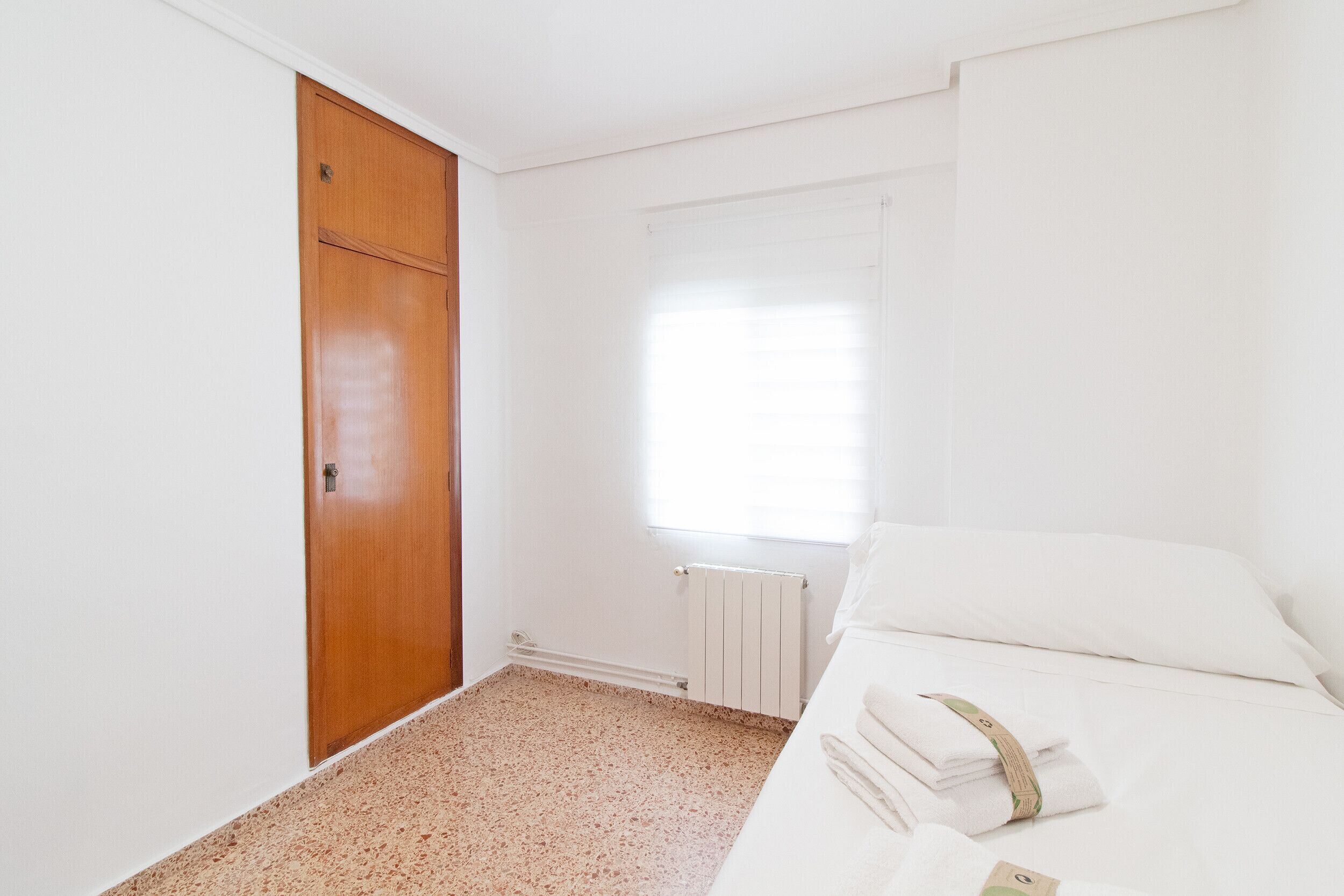 Un dormitorio con cama, un armario de madera, un radiador y una ventana con persianas.