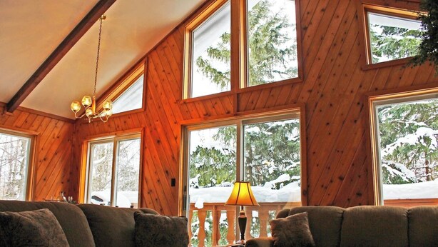 A cozy cabin interior with wooden walls, large windows, and a sofa.