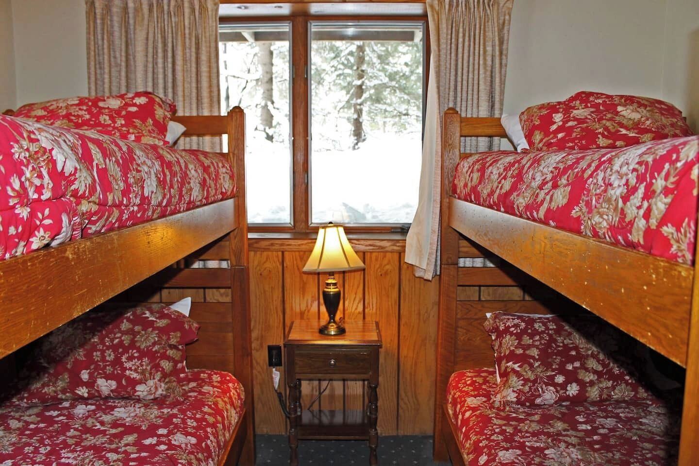Une chambre avec deux lits superposés, une petite table avec une lampe et une fenêtre avec des rideaux.