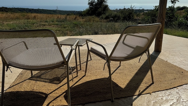 Two metal chairs with mesh backs and beige cushions, a small table, and a woven mat on a concrete patio overlooking a coastal landscape. - Loft relaxation in the hills (Lazio)