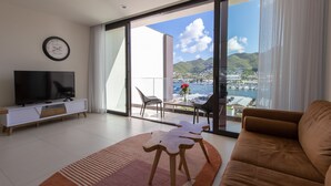 A modern living room with a large TV, a sofa, a dining table with chairs, and a view of a marina and mountains. - A134 - Panoramic View of the Lagoon (Sint Maarten)