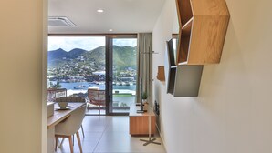 A modern room with a dining area, a TV mounted on the wall, and a view of a marina and mountains. - A116 - Immersive Simpson Bay Lagoon View (Sint Maarten)