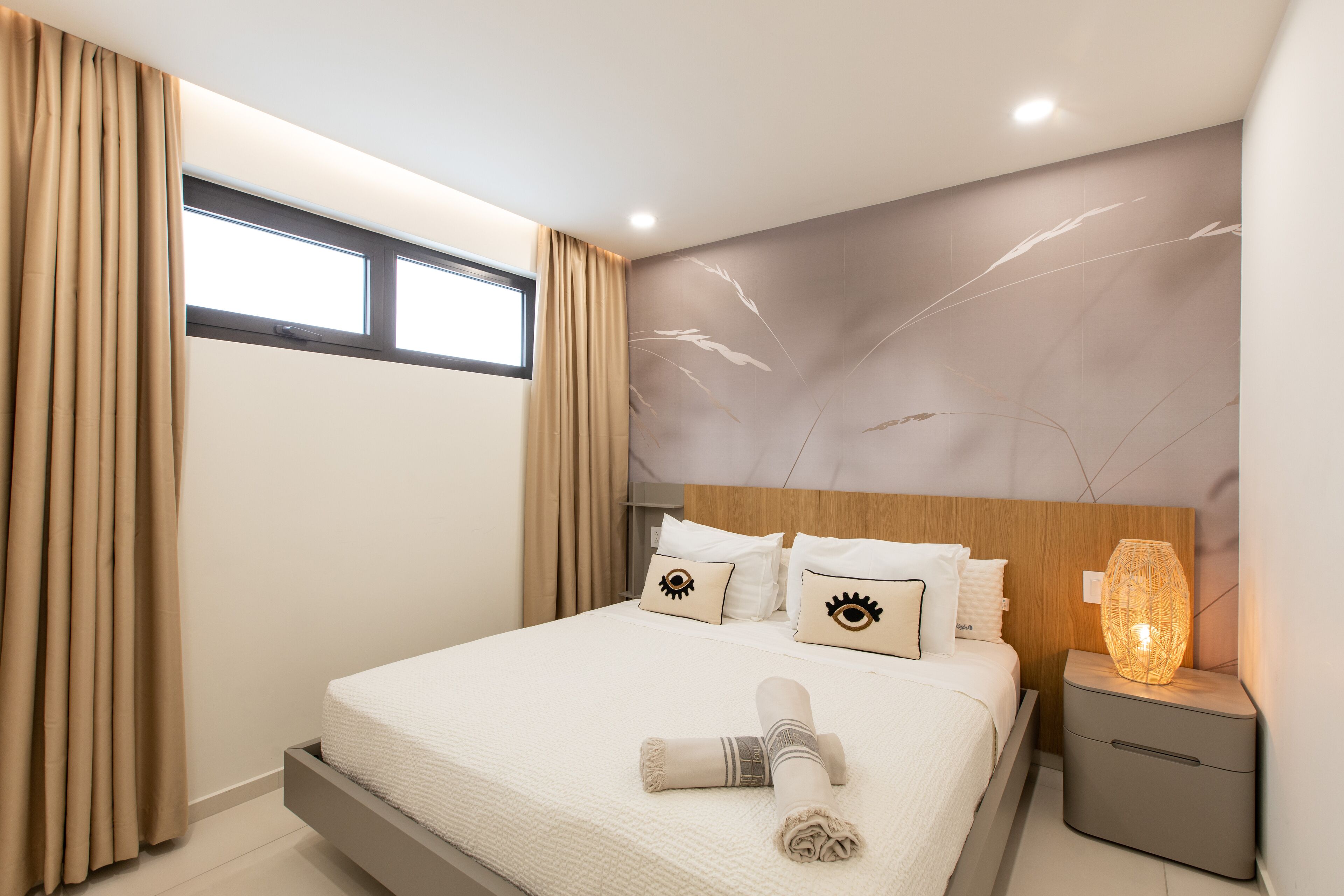 Ein modernes Hotelzimmer mit Bett, Vorhängen, Nachttisch und Wandlampe.