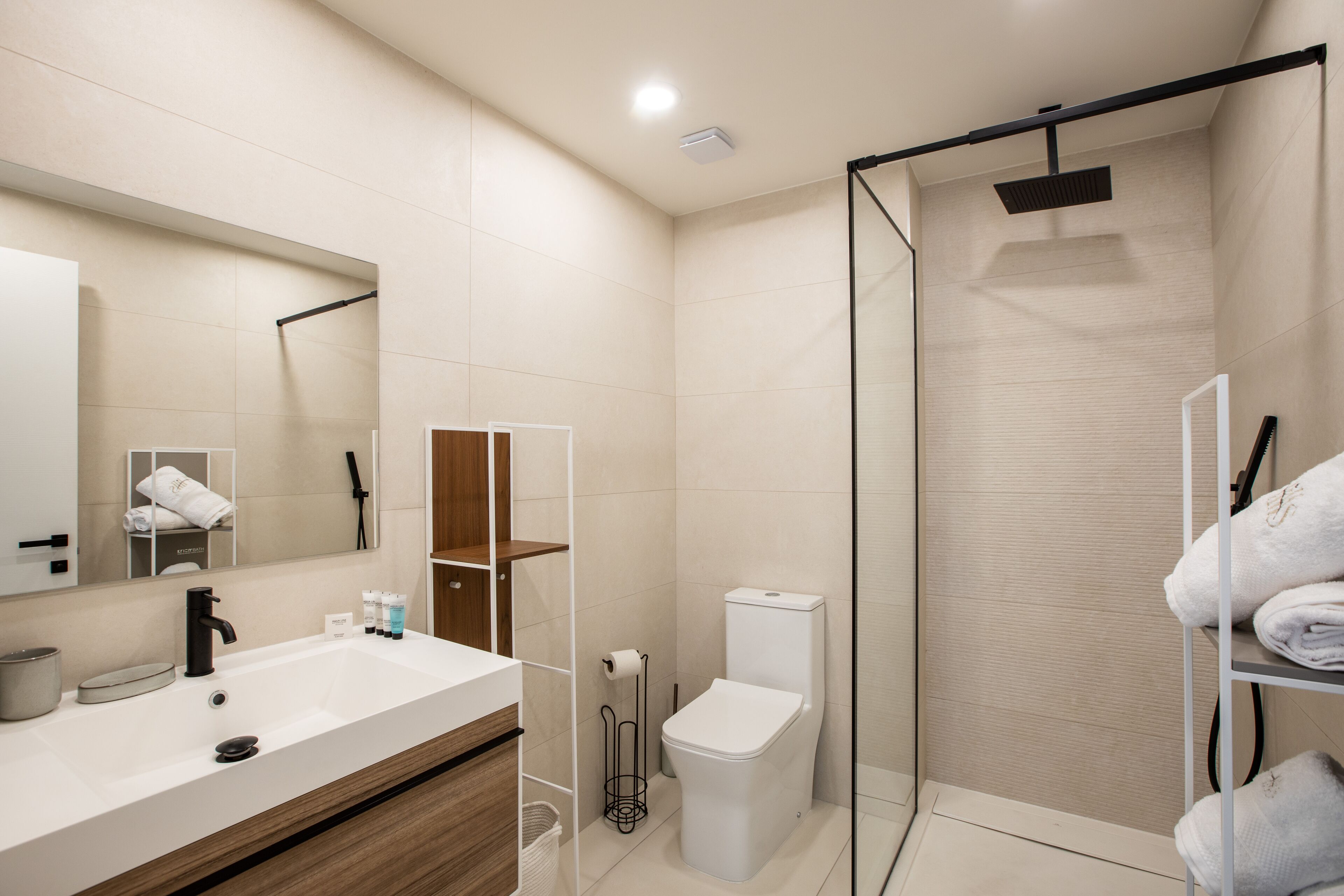 A modern bathroom with a large mirror, a white sink, a toilet, and a glass shower enclosure.