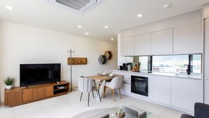A modern living room with a flat-screen TV, a dining area with a wooden table and chairs, a glass coffee table, and a sofa. - A116 - Immersive Simpson Bay Lagoon View (Sint Maarten)