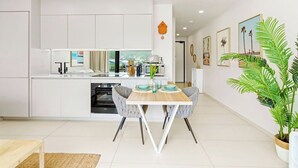 Une cuisine moderne avec des meubles blancs, un îlot central et un coin repas comprenant une table et des chaises en bois.