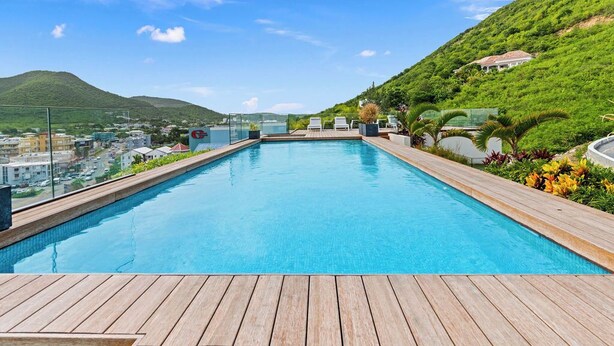 Une piscine dotée d’une terrasse en bois, entourée de verdure et située au pied d’une colline.