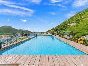 A swimming pool with a wooden deck, surrounded by greenery and a hillside. - A101 - Outstanding Lagoon View & Garden (Sint Maarten)