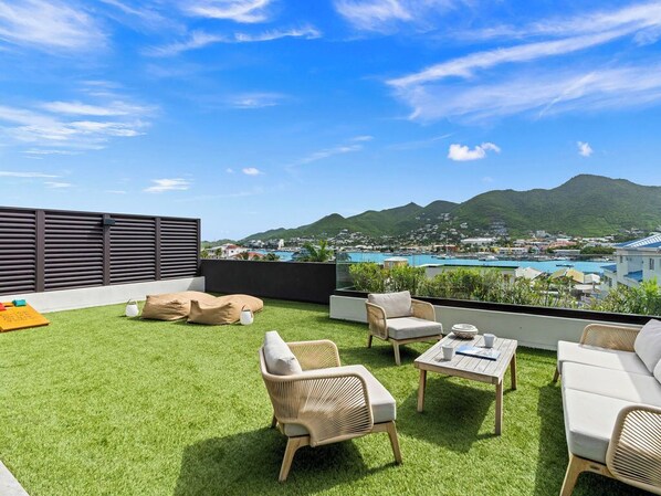A rooftop terrace with outdoor furniture, a view of a mountain, and a pool in the background. - A101 - Outstanding Lagoon View & Garden (Sint Maarten)