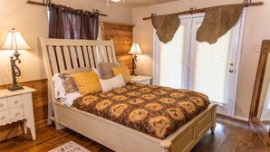 Een slaapkamer met een houten bed, twee nachtkastjes met lampen, een raam met gordijnen en een houten vloer.