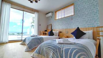 A hotel room with two beds, a large window with a view, a wooden headboard, and a ceiling light fixture.