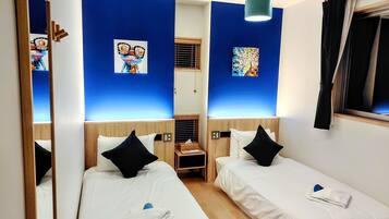 A hotel room with two single beds, a wooden wardrobe, a small desk, and a mirror.
