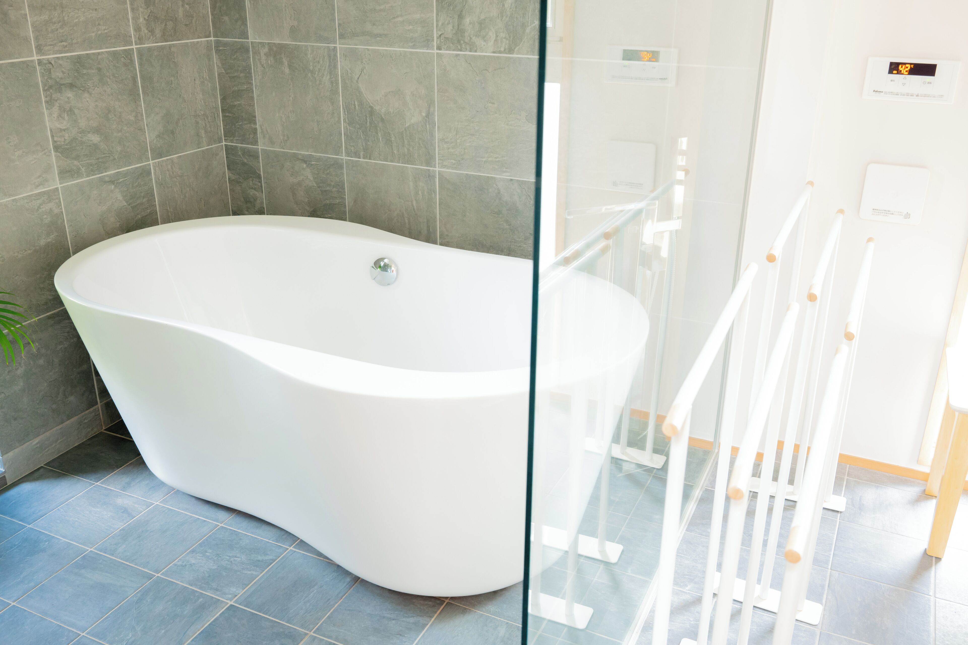 A modern bathroom with a freestanding bathtub, grey tiled walls, and a glass partition.