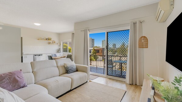 Relax in this stylish living room with a comfortable sofa, coffee table, and dining area, offering a view of the city skyline from the balcony.