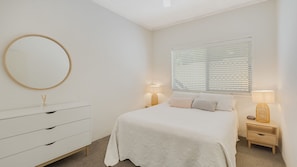 Relax in a serene space with a large round mirror, a comfortable bed, and a bedside table with a lamp.