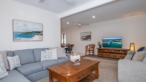 Uma sala de estar com um sofá cinzento, uma mesa de centro de madeira e uma televisão sobre um suporte de madeira.