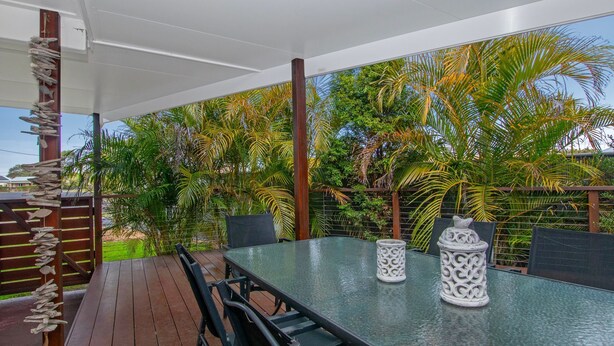 Pátio externo com mesa de vidro, dois castiçais brancos e cerca de madeira decorada com enfeites de peixes.