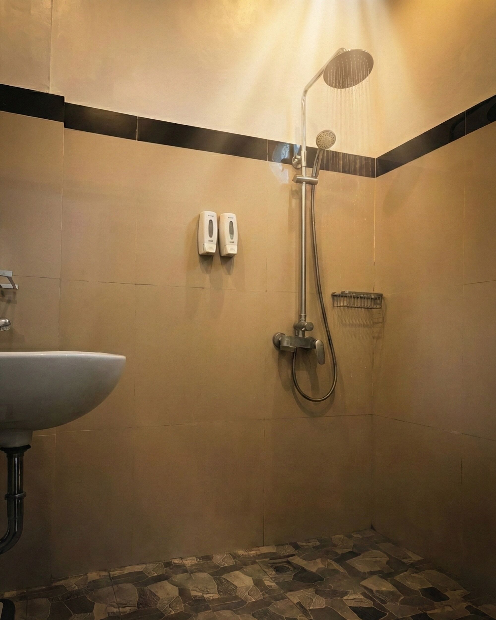 Casa de banho com chuveiro, pia e dois dispensadores de sabonete na parede.