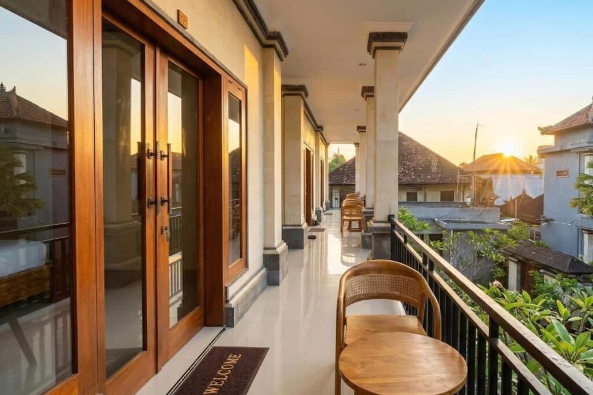 Un pasillo de hotel con felpudo, puertas de madera y un balcón con mesa y sillas.