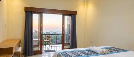 A hotel room with a bed, a desk, and a balcony with a view.