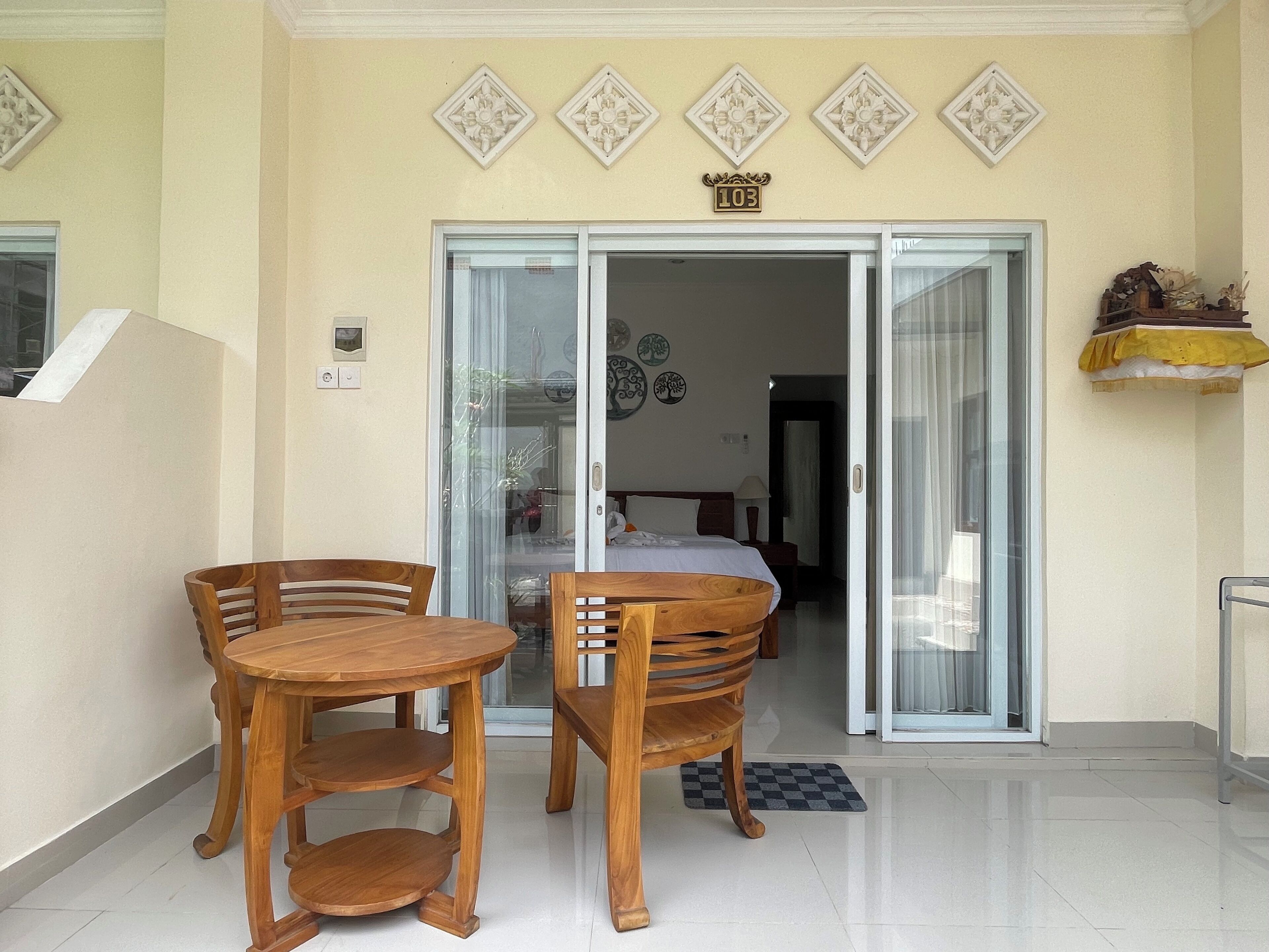 A hotel entrance with a wooden table and chairs, a sliding glass door, and a number sign above the door.