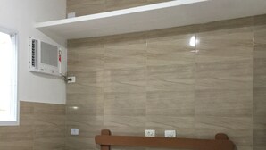Un dormitorio con cama de madera, colchón blanco, aire acondicionado de pared y una ventana.
