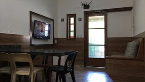 Un comedor con una mesa y sillas, un televisor montado en la pared y una puerta corrediza que da a un balcón.