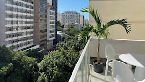 A balcony with a potted palm tree, white chairs, and a table. - Precioso Apartamento con Terraza y Piscina (Ipanema Rio de Janeiro)