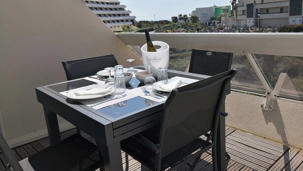 A dining table set for two on a balcony with a clear view of the cityscape. - Studio Heliopolis K Int. Naturist Village AC/Park (Agde)