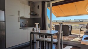 A compact kitchen with a dining area, a large sliding glass door leading to an outdoor patio. - Studio Heliopolis K Int. Naturist Village AC/Park (Agde)