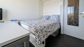 A small, modern room with a bed, a desk, and a door. - Studio Heliopolis K Int. Naturist Village AC/Park (Agde)