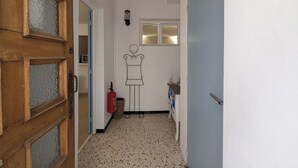 Ein schmaler Flur mit einer Holztür links, einer weißen Wand mit einem Fenster und einem kleinen Fenster rechts.