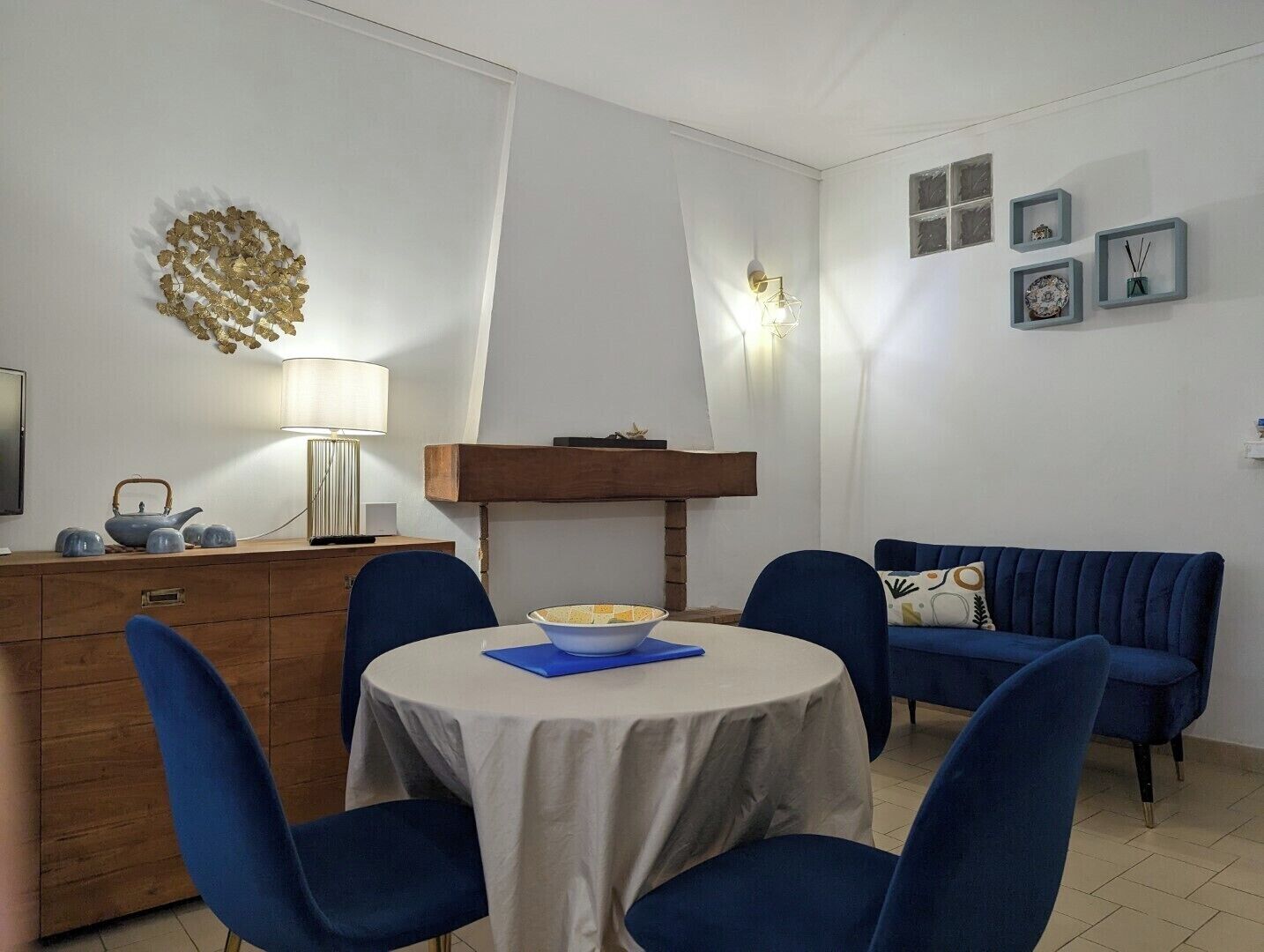A dining area with a round table, blue chairs, a wooden sideboard, and a blue sofa.
