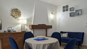 Ein Essbereich mit einem runden Tisch, blauen Stühlen, einer Holzkommode und einem blauen Sofa.