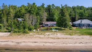 Ein Küstengrundstück mit Sandstrand, einem kleinen Haus mit Terrasse und dichtem Wald im Hintergrund.