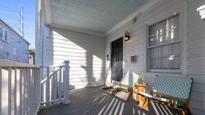 A covered porch with a wooden bench and a small table, white siding, and a window with blinds.