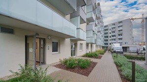 Ein modernes Apartmenthaus mit gepflastertem Gehweg, Glasbalkonen und einem Baukran im Hintergrund.